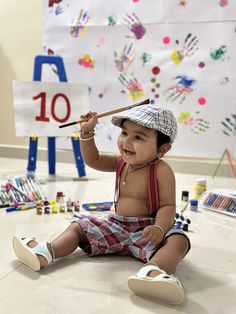 a baby sitting on the floor holding a paintbrush