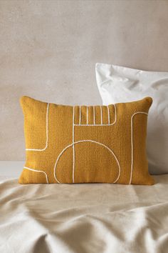 a yellow pillow sitting on top of a bed next to a white pillow cover and pillows