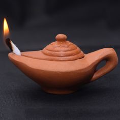 a small clay teapot with a lit candle in it