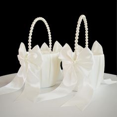 two white bags with bows and pearls on them sitting on top of a table next to each other