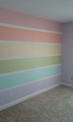 an empty room with pastel stripes painted on the wall and carpeted flooring