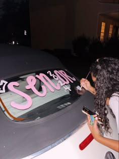 a woman is painting the side of a car with pink letters and writing on it