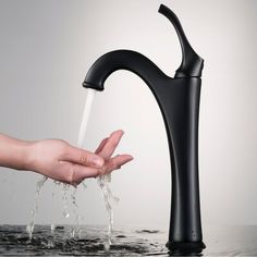 a person's hand under a black faucet with water pouring from it