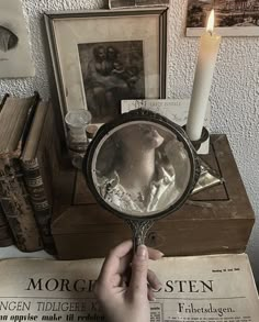 a person holding a magnifying glass in front of an old book and candle