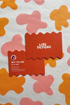 two red business cards sitting on top of a pink and orange pattern paper covered surface