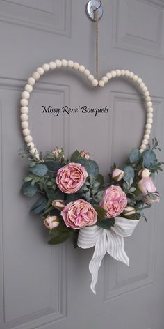 a heart shaped wreath with pink roses and greenery hanging on the front door,