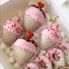 ice cream cones decorated with pink frosting and sprinkles in a box