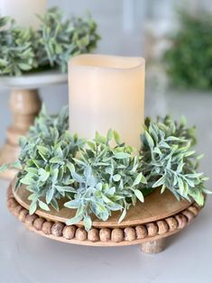 a lit candle sitting on top of a table next to some potted greenery