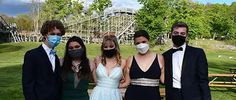 four people wearing face masks in front of a roller coaster