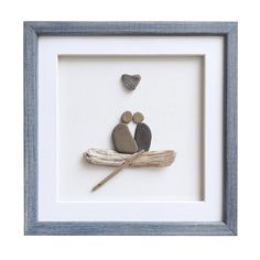 two pebbles sitting on a piece of driftwood in a shadow box frame