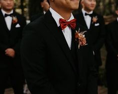 a group of men standing next to each other wearing suits and bow ties with trees in the background