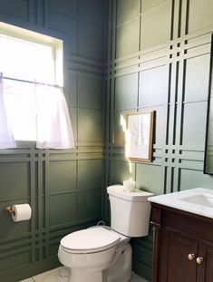 a white toilet sitting next to a sink in a bathroom under a window with green paneling