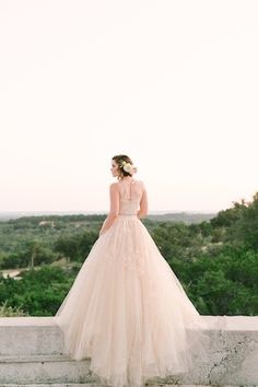 a woman in a wedding dress standing on some steps looking out at the trees and bushes