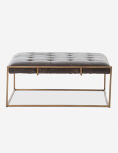 an upholstered bench with metal legs and a leather cushion on the bottom, in front of a white background