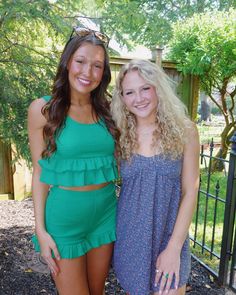 two beautiful young women standing next to each other in front of a fence and trees