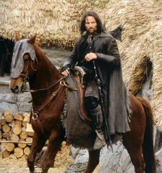 a man riding on the back of a brown horse next to a pile of hay