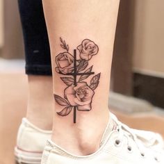 a woman's foot with a cross and roses tattoo on the side of her leg