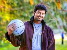 a man holding a basketball in his right hand and smiling at the camera while standing outside