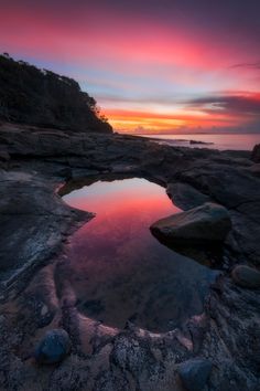 the sun is setting over some rocks and water