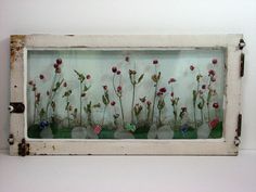 an old window with flowers in it is hanging on the wall next to a white wall