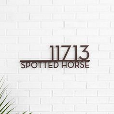 a white brick wall with a metal sign that reads 11 / 13 spotted horse on it