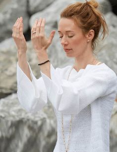 a woman standing in front of rocks holding her hands up to the side while wearing a white sweater