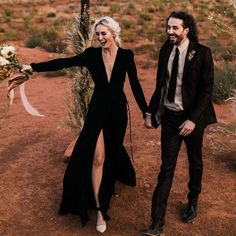 a man and woman holding hands while walking through the desert with flowers in their hand