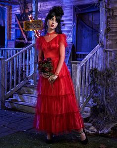 a woman in a red dress is standing on the porch with her bouquet and looking at the camera