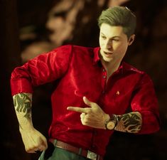 a man in a red shirt pointing at something with his finger and arm tattoos on