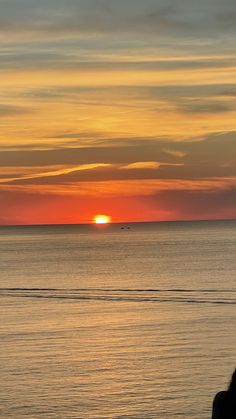 the sun is setting over the ocean and people are walking on the beach