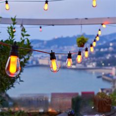 several light bulbs hanging from a string over a table with water and mountains in the background