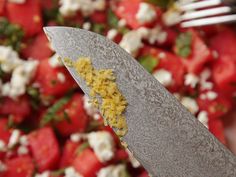 a knife with some food on top of it next to a bowl of tomatoes and feta cheese