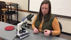 a woman sitting at a table in front of a microscope