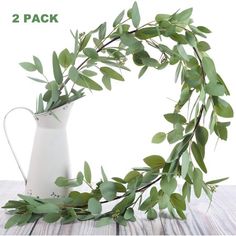 a white vase with some green leaves in it on a wooden table next to a metal watering can