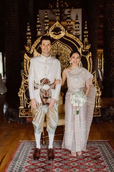 a man and woman standing next to each other in front of a gold throne on a rug