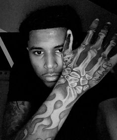 a black and white photo of a man with tattoos on his arms, holding his hand up to the camera