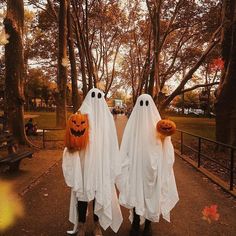 two people dressed up as ghostes with pumpkins on their heads in the park