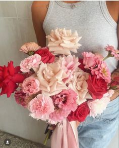 a woman holding a bouquet of flowers in her hands and wearing a gray tank top