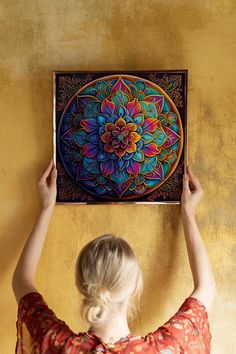 a woman is holding up a painting on the wall above her head and looking at it