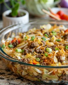 a glass bowl filled with noodles, meat and veggies on top of a table