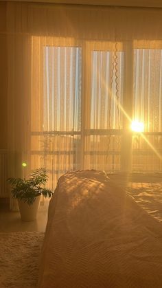 the sun shines brightly through sheer curtains in a bedroom with a bed and plant