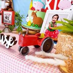 a table topped with cake and farm animals next to a red tractor on top of a checkered table cloth