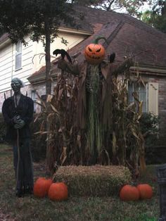 two scarecrows are standing in front of a house with pumpkins and hay