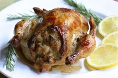 a whole chicken on a plate with lemons and rosemary