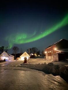 an aurora bore is seen in the night sky over houses and snow covered ground with lights on