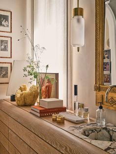 a wooden dresser topped with a vase filled with flowers next to a mirror and lamp