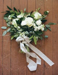 a bouquet of white roses and greenery tied to a wooden floor with ribbon on it