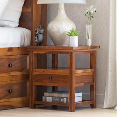 a nightstand with two drawers and a lamp next to it on top of a bed