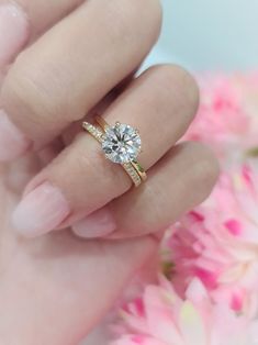 a woman's hand holding a ring with a diamond on it and pink flowers in the background