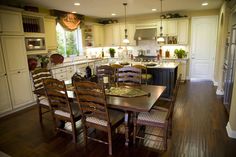 a dining room table and chairs in a kitchen with white cabinets, wood floors and an island